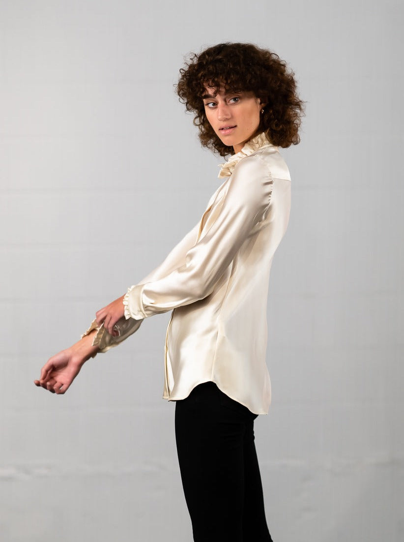 Model wearing Marabilis silk blouse in ivory with ruffel collar, showing side  seams.