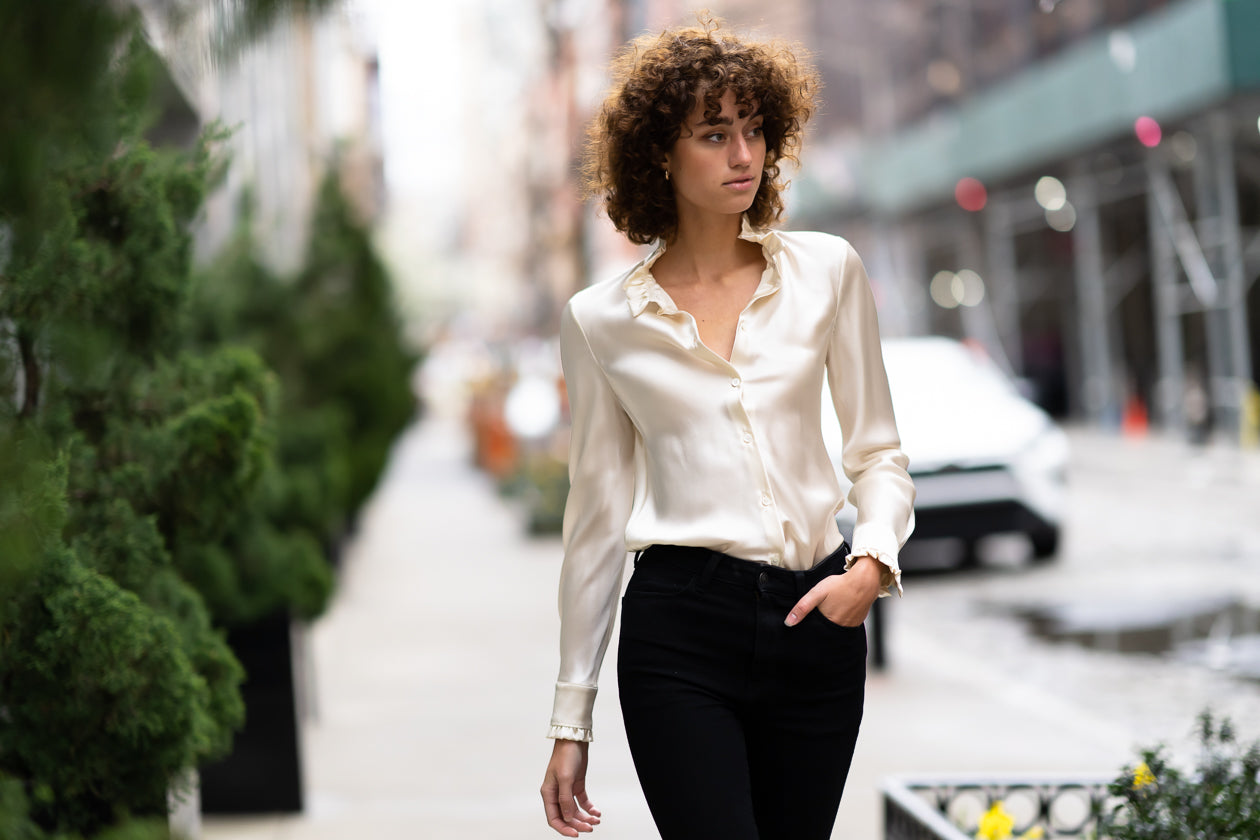 Model walking on street wearing Marabilis silk satin blouse in ivory with ruffle collar in Gabrielle style in 